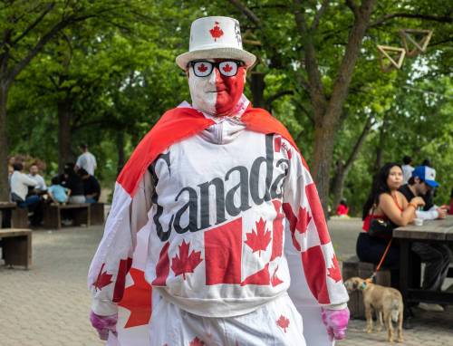 Photo by Maryrose Villena
                                A man at The Forks walking around the area while wearing a full-on Canada costume: flag as a cape, face paint, and sweatshirt with Canada printed on it on July 1.
