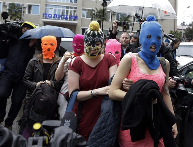 Five women wearing balaclavas, two of whom are members of the Russian punk group Pussy Riot, make their way through a crowd after they were released from a police station, Tuesday, Feb. 18, 2014, in Adler, Russia. No charges were filed against the Pussy Riot members Nadezhda Tolokonnikova, in the blue balaclava, and Maria Alekhina, in the pink, who were held along with several other people near the city's ferry terminal. (AP Photo/Morry Gash)