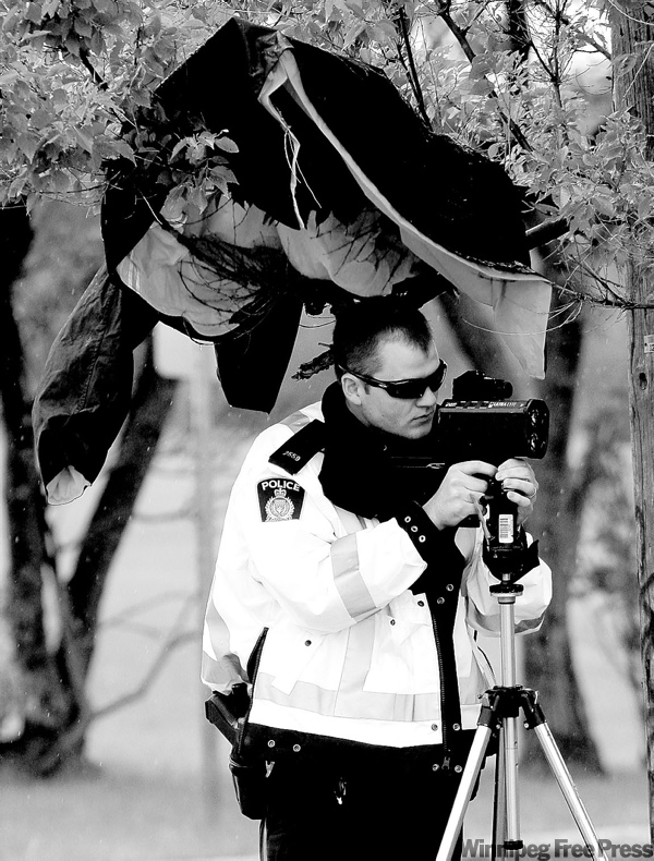 KEN GIGLIOTTI / WINNIPEG FREE PRESS
A member of the police traffic division mans a speed trap on Kenaston Boulevard under a makeshift rain shelter Monday.