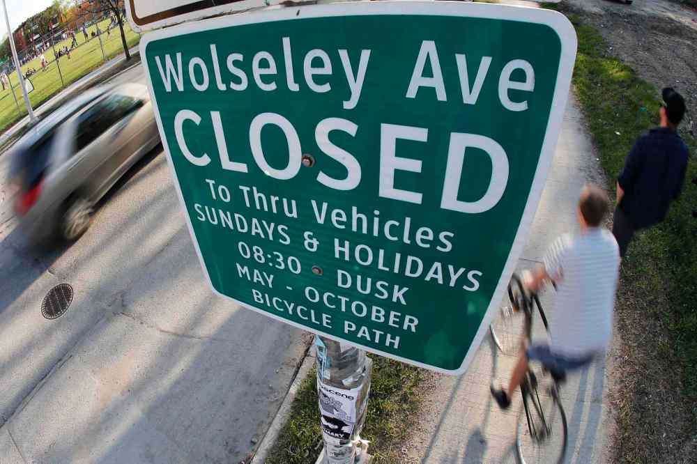 John Woods / Winnipeg Free Press
Cars, pedestrians, cyclists and pedestrians pass signage on Wolseley Avenue indicating Sunday and holiday street closure.