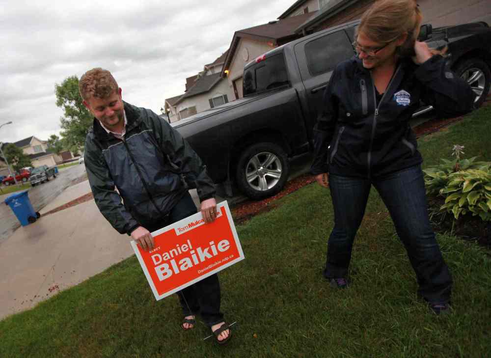 Daniel Blaikie pushes a campaign sign into a transcona lawn Wednesday evening assisted by Breigh Kusmack. The sign at 171 Chadwick Cr. was the first in the area. (Phil Hossack / Winnipeg Free Press)