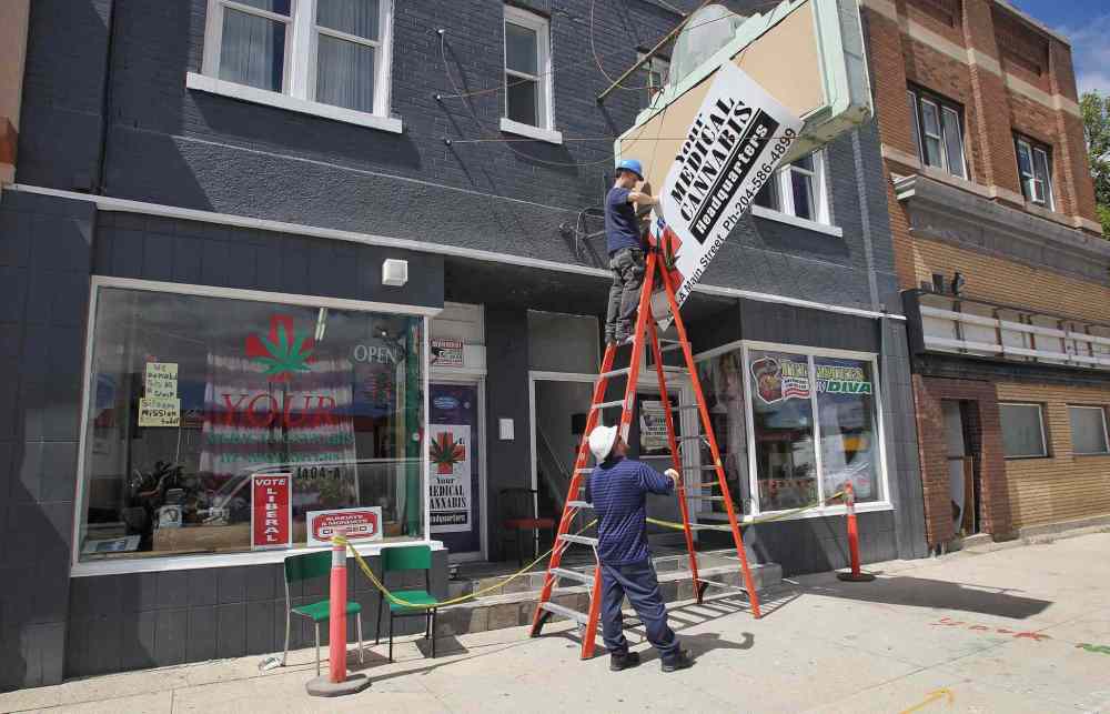 A city contractor removes the sign at the Main Street store that was selling marijuana. The store owner was arrested Tuesday afternoon. (Mike Deal / Winnipeg Free Press)