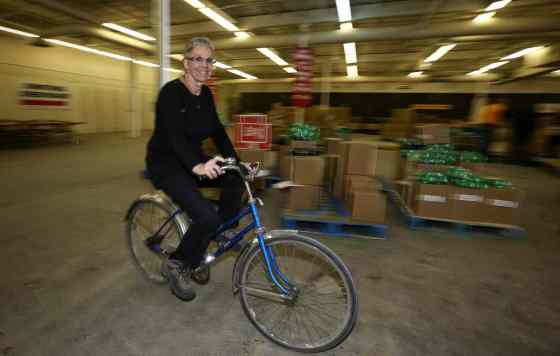Mike Deal / Winnipeg Free PressLinda Grayston the assistant executive director for the Christmas Cheer Board rides around the warehouse on a blue bike.