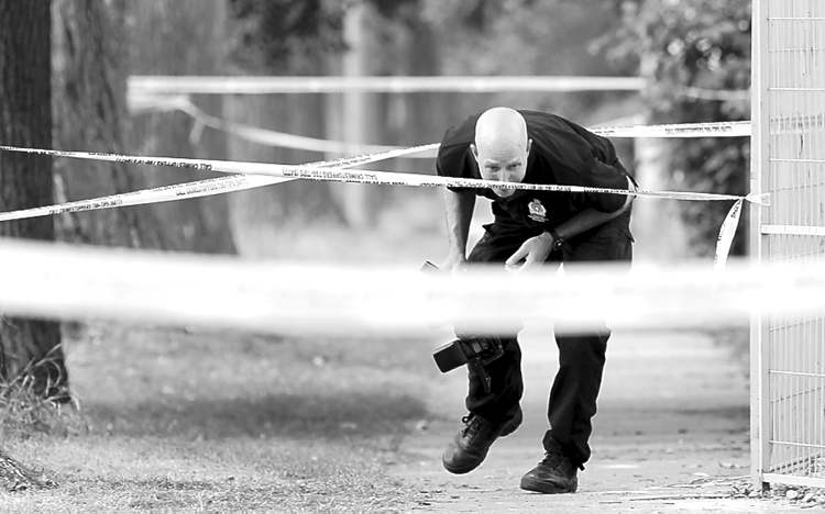 Wayne Glowacki / Winnipeg Free Press archives
An identification-unit officer ducks under tape at the crime scene earlier this month.