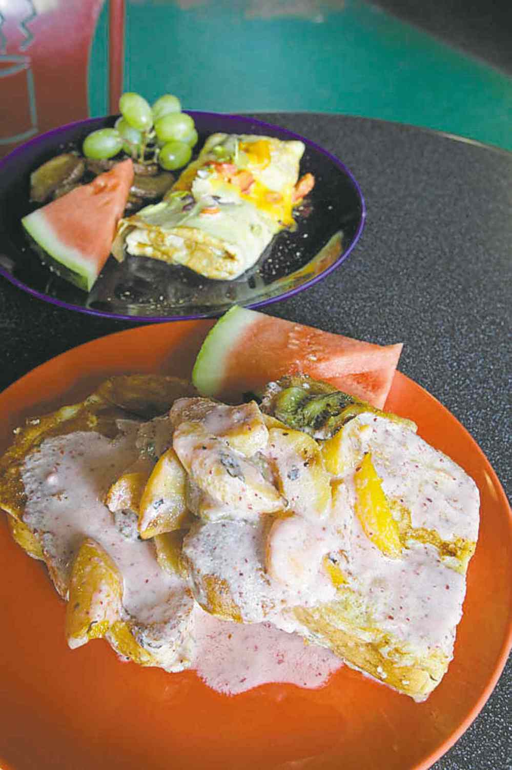 Two breakfast dishes served at X-Cues are French toast with peaches in fruit purée (foreground) and veggie omelettes.