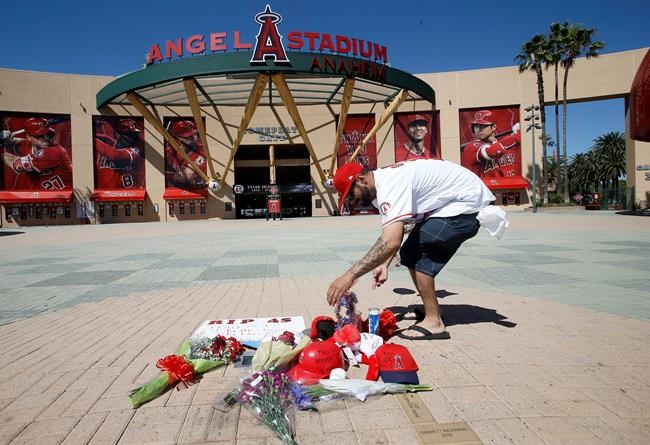Los Angeles Angels fan Steven Beltran adds to a makeshift memorial at Angels Stadium in Anaheim, Calif., for pitcher Tyler Skaggs, who died Monday at the age of 27, in Texas, stunning Major League Baseball and leading to the postponement of the team's game against the Texas Rangers Monday, July 1, 2019. (AP Photo/Alex Gallardo)