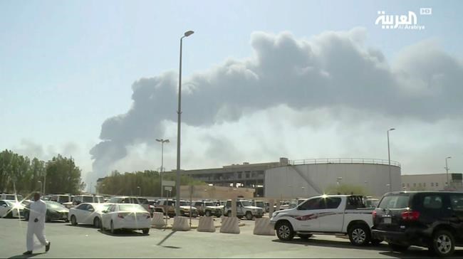 In this image made from a video broadcast on the Saudi-owned Al-Arabiya satellite news channel on Saturday, Sept. 14, 2019, a man walks through a parking lot as the smoke from a fire at the Abqaiq oil processing facility can be seen behind him in Buqyaq, Saudi Arabia. Drones launched by Yemen's Houthi rebels attacked the world's largest oil processing facility in Saudi Arabia and another major oilfield Saturday, sparking huge fires at a vulnerable chokepoint for global energy supplies. (Al-Arabiya via AP) TV OUT NO SALES