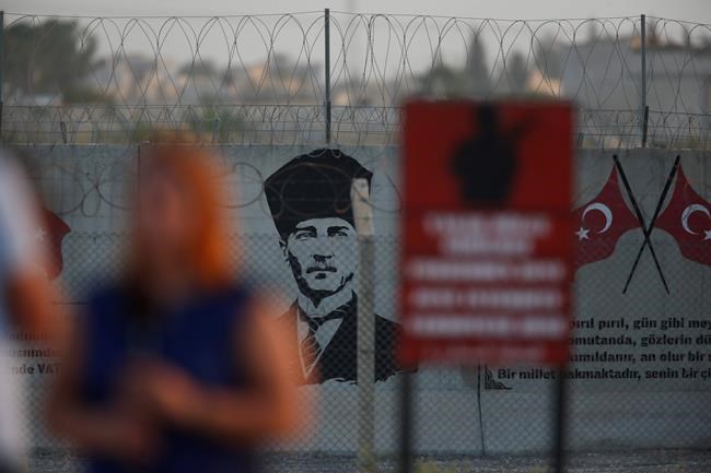 A graffiti of modern Turkey's founder Mustafa Kemal Ataturk is seen on the Turkish side of the border between Turkey and Syria, as a TV journalist works in Akcakale, Sanliurfa province, southeastern Turkey, Tuesday, Oct. 8, 2019. The Turkey - Syria border has became a hot spot as Turkish Vice President Fuat Oktay said Turkey was intent on combatting the threat of Syrian Kurdish fighters across its border in Syria.(AP Photo/Lefteris Pitarakis)