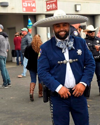 In this July 18, 2019 photo, wearing a traditional Mexican charro outfit, Salinas Police Officer Robert Hernandez does outreach at the California Rodeo Salinas in Salinas, Calif. The police department in a largely Latino Northern California city is reaching out to the community in a new way, a police uniform that resemble the traditional Mexican charro suit. Two Salinas police officers wore a blue suede charro suit embellished with silver embroidery, a blue and white bow and topped by a white sombrero to the city's annual rodeo, drawing lines of men, women and children who wanted a photo with them, the Salinas Californian reported Thursday, July 25, 2019. (Kate Cimini/The Californian via AP)