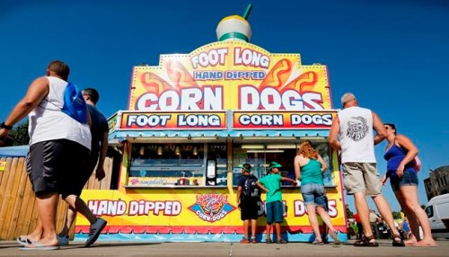 FILE - In this Aug. 9, 2018 file photo, Iowa State fairgoers line up to get a corn dog at a concession stand during the opening day of the Iowa State Fair in Des Moines, Iowa. The Iowa State Fair has confirmed that it will require all food and drink vendors to accept credit and debit card payments beginning in 2020. Cash has long been the dominant method of payment for the fried cheese curds, corn dogs, and scores of other foods bought by fairgoers. (AP Photo/Charlie Neibergall, File)