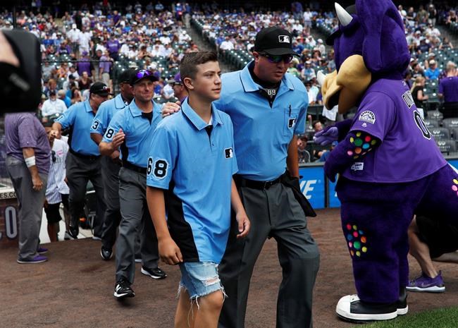 Thirteen-year-old Josh Cordova, left, of Denver, heads on the diamond with home plate umpire Cory Blaser before the Colorado Rockies host the Los Angeles Dodgers in the first inning of a baseball game Sunday, June 30, 2019, in Denver. The young man was officiating a youth baseball game when a brawl broke out among adults in the nearby suburb of Lakewood, Colo. (AP Photo/David Zalubowski)