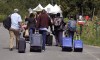 A family from Haiti approach a tent in Saint-Bernard-de-Lacolle, Quebec, stationed by Royal Canadian Mounted Police, as they haul their luggage down Roxham Road in Champlain, N.Y., on August 7, 2017. Quebecers living near the Canada-United States border, where thousands of migrants have crossed irregularly into the country since 2017, will receive more than $400,000 to compensate them for increased traffic and noise. THE CANADIAN PRESS/AP, Charles Krupa