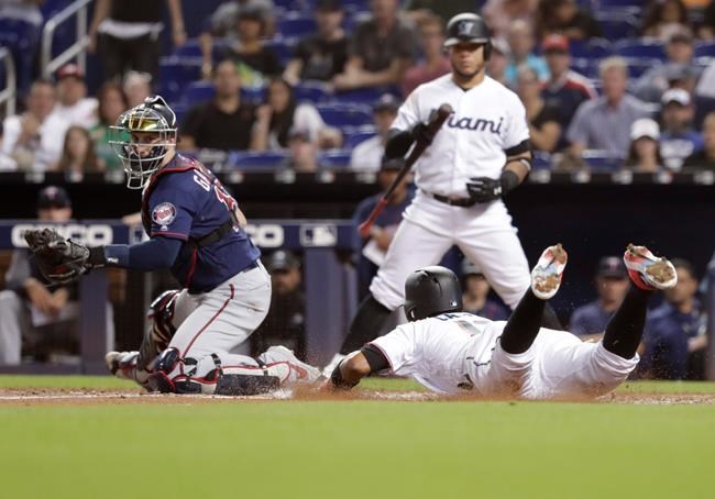 Minnesota Twins catcher Mitch Garver, left, watches as Miami Marlins' Starlin Castro scores on a double by Curtis Granderson during the fourth inning of a baseball game Tuesday, July 30, 2019, in Miami. (AP Photo/Lynne Sladky)