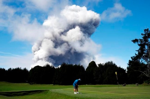 ADVANCE FOR RELEASE FRIDAY, MAY 3, 2019 AT 12:01 A.M. EDT AND THEREAFTER. FILE - In this May 21, 2018 file photo, Doug Ralston plays golf in Volcano, Hawaii, as a huge ash plume rises from the summit of Kiluaea volcano. A year after the Hawaii volcano rained lava and gases on a rural swath of the Big Island in one of its largest and most destructive eruptions in recorded history, people who lost their homes and farms in the disaster are still struggling to return to their island lifestyle. (AP Photo/Jae C. Hong, File)