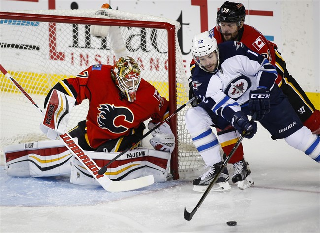 Winnipeg Jets' Drew Stafford, centre, tries for a lose puck as Calgary Flames' Deryk Engelland defends and goalie Joni Ortio, left, from Finland, looks on during first period NHL hockey action in Calgary, Wednesday, March 16, 2016.THE CANADIAN PRESS/Jeff McIntosh