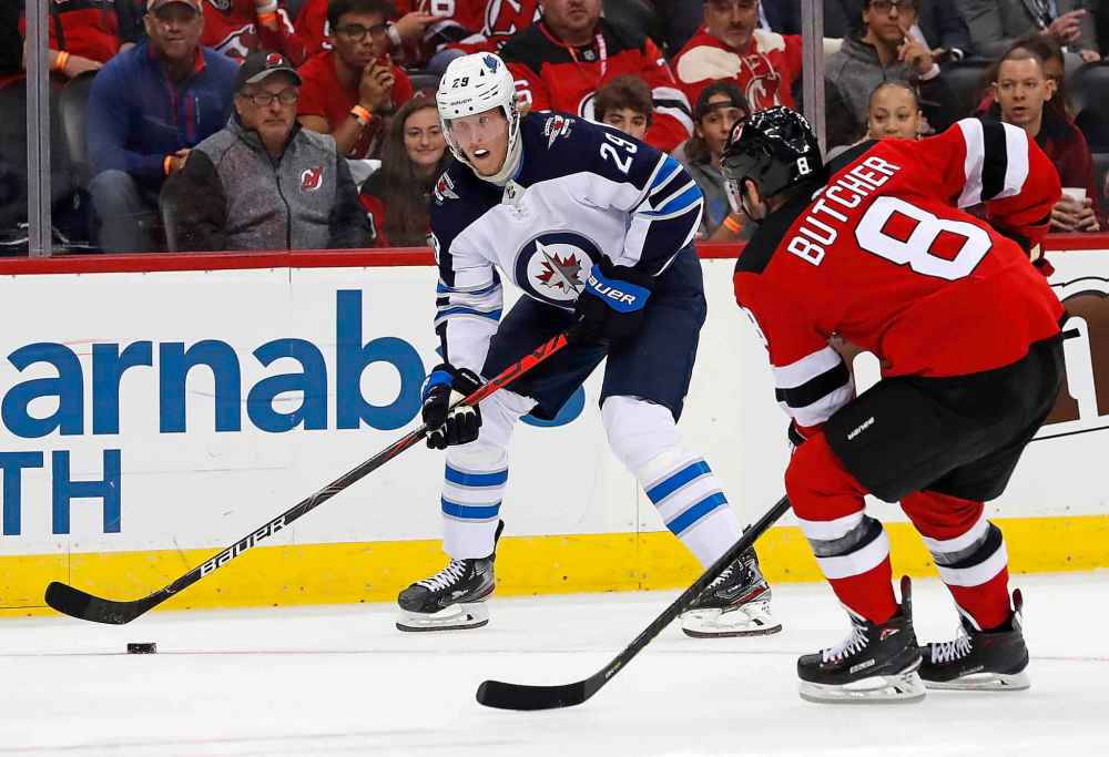 Patrik Laine plays the puck against Will Butcher during the first period. Laine got an assist later on in the night on Mathieu Perreault's goal. (Noah K. Murray / The Associated Press)