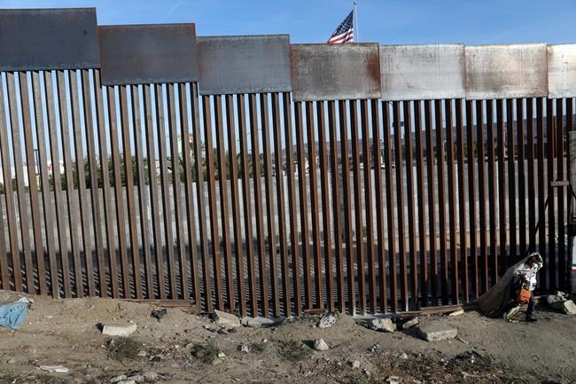 FILE - In this Nov. 21, 2018, file photo, a homeless man walks next to the fence that divides Mexico and the U.S, in Tijuana, Mexico. The Trump administration expects to launch a policy as early as Friday, Jan. 25, 2019, that forces people seeking asylum to wait in Mexico while their cases wind through U.S. courts, an official said, marking one of the most significant changes to the immigration system of Donald Trump's presidency. (AP Photo/Rodrigo Abd, File)
