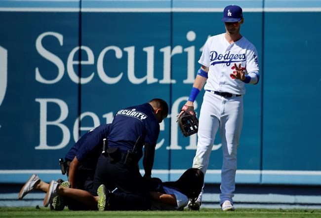 Los Angeles Dodgers right fielder Cody Bellinger, right, waves to a fan that ran out to him as she is handcuffed during the ninth inning of a baseball game against the Colorado Rockies, Sunday, June 23, 2019, in Los Angeles. (AP Photo/Mark J. Terrill)