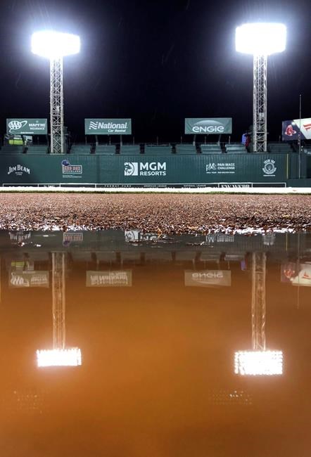 Stadium lights are reflected in a puddle on the warning track in front of the Boston Red Sox dugout in a break from heavy rain during a weather delay with the score tied 4-4 in the 10th inning of the Red Sox's baseball game against the Kansas City Royals at Fenway Park in Boston, Wednesday, Aug. 7, 2019. (AP Photo/Charles Krupa)