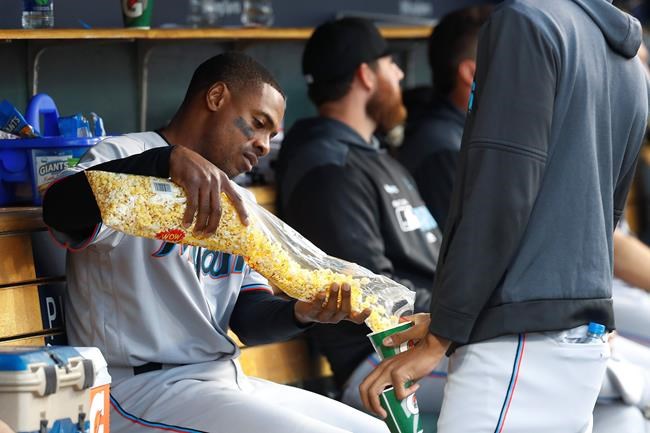 Miami Marlins' Curtis Granderson, left, shares popcorn with a teammate in the dugout during the third inning of the team's baseball game against the Detroit Tigers in Detroit, Tuesday, May 21, 2019. (AP Photo/Paul Sancya)