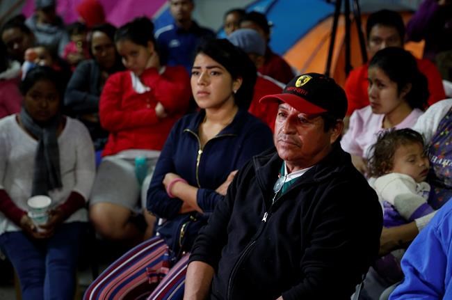 Migrants mainly from Mexico and Central America look on as U.S. President Donald Trump gives a prime-time address about border security on television, Tuesday, Jan. 8, 2019, watching from a border migrant shelter in Tijuana, Mexico. (AP Photo/Gregory Bull)