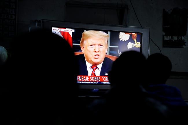 Migrants mainly from Mexico and Central America look on as U.S. President Donald Trump gives a prime-time address about border security Tuesday, Jan. 8, 2019, watching from a border migrant shelter in Tijuana, Mexico. (AP Photo/Gregory Bull)
