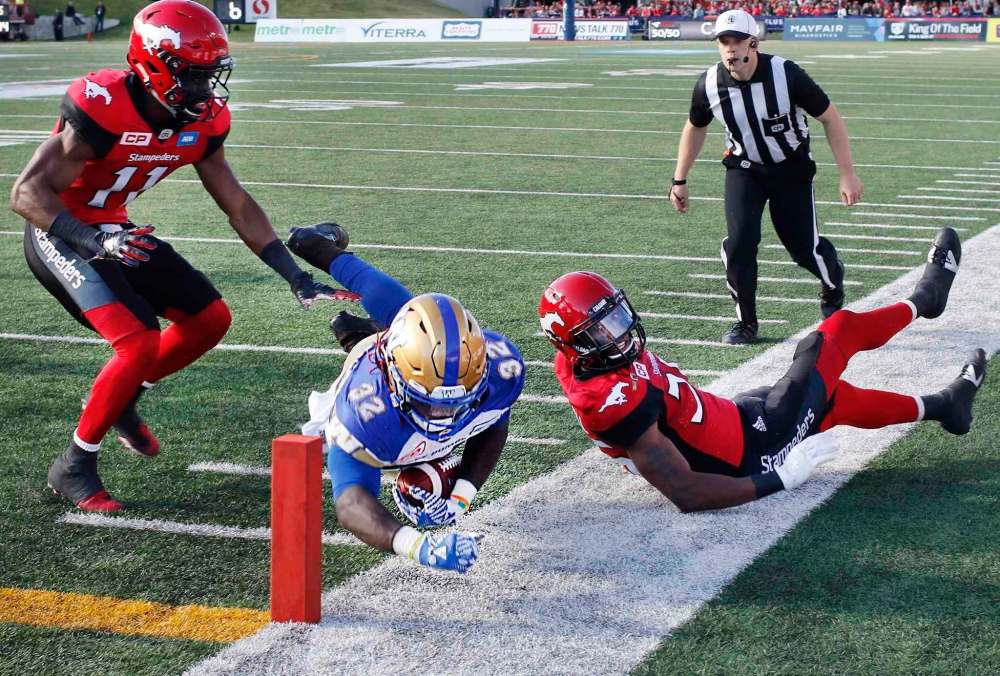 Winnipeg Blue Bombers' Timothy Flanders, centre, is knocked out of bounds at the one yard line by Calgary Stampeders' Joshua Bell, left, and Tommie Campbell during second half CFL football action, in Calgary on Saturday, Sept. 24, 2016. THE CANADIAN PRESS/Larry MacDougal