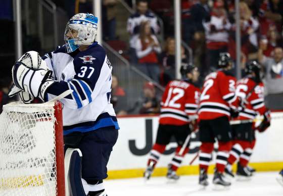 Winnipeg Jets goalie Connor Hellebuyck (37) stands on his net as New Jersey Devils players celebrate a goal by Stefan Noesen (23) during the second period of an NHL game, Tuesday, March 28, 2017, in Newark, N.J. (AP Photo/Julio Cortez)