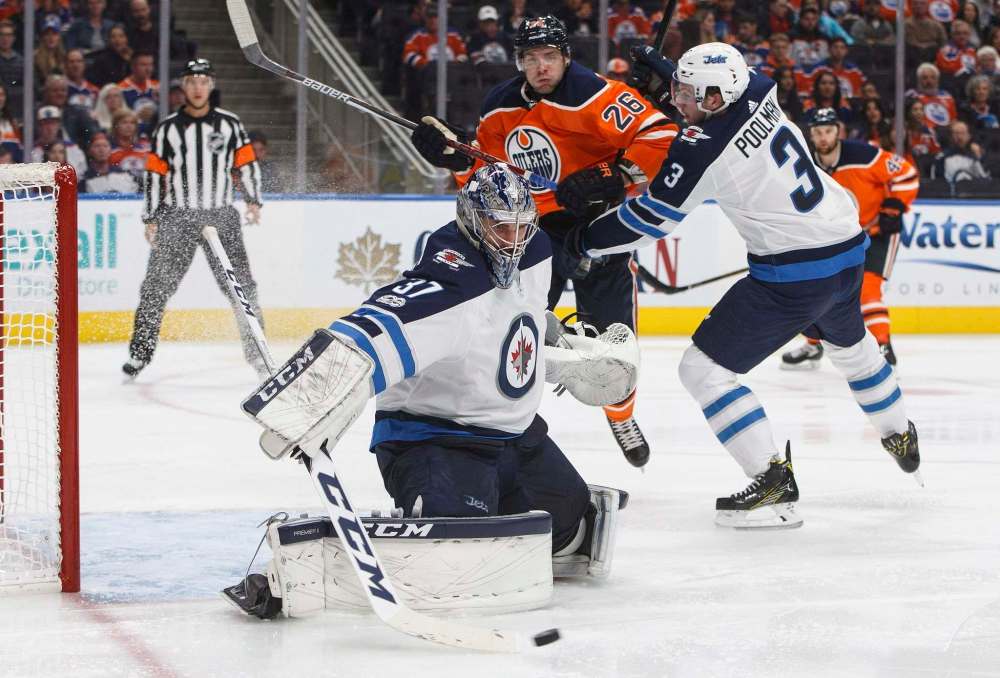 THE CANADIAN PRESS/Jason Franson
Winnipeg Jets goalie Connor Hellebuyck makes a save as Edmonton Oilers' Iiro Pakarinen and Tucker Poolman battle in front of the net during second period NHL action in Edmonton, Monday. Poolman drew into his first regular season NHL game as a result of an injury to veteran blue-liner Dustin Byfuglien.
