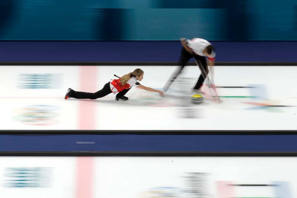 Canada's Kaitlyn Lawes throws a stone as teammate John Morris begins to sweep ice during the mixed doubles curling match Saturday. (Aaron Favila / The Associated Press)
