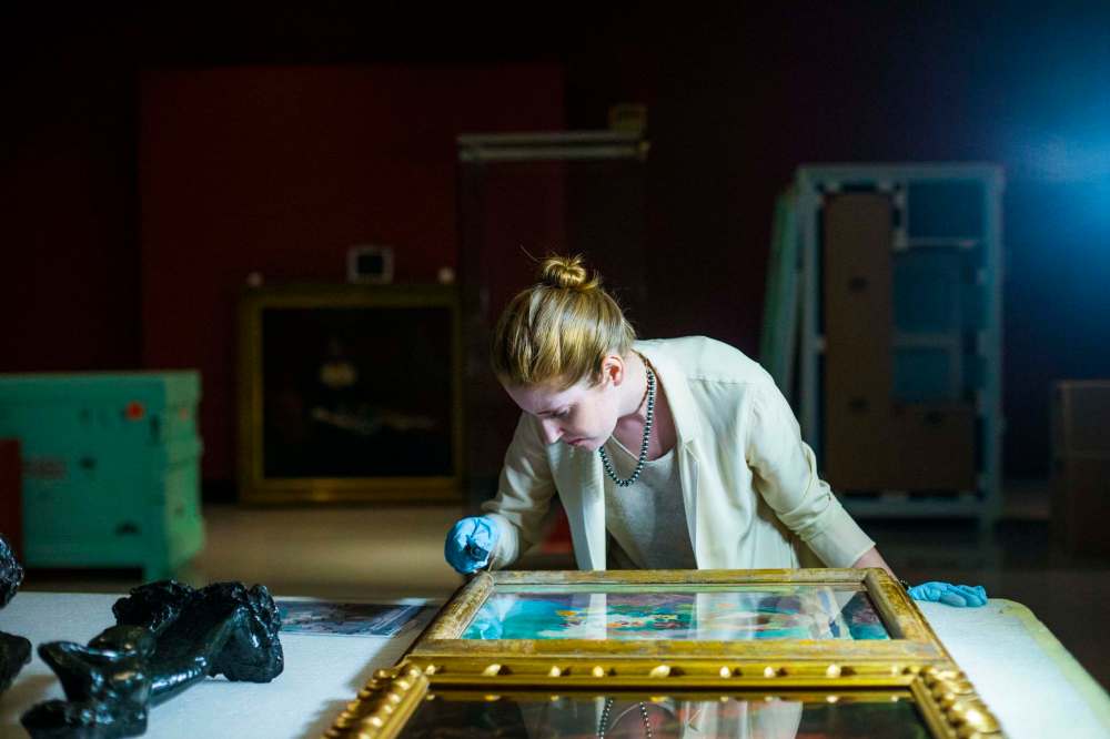 Conservator Erin Anderson inspects paintings as they are uncrated at the gallery.