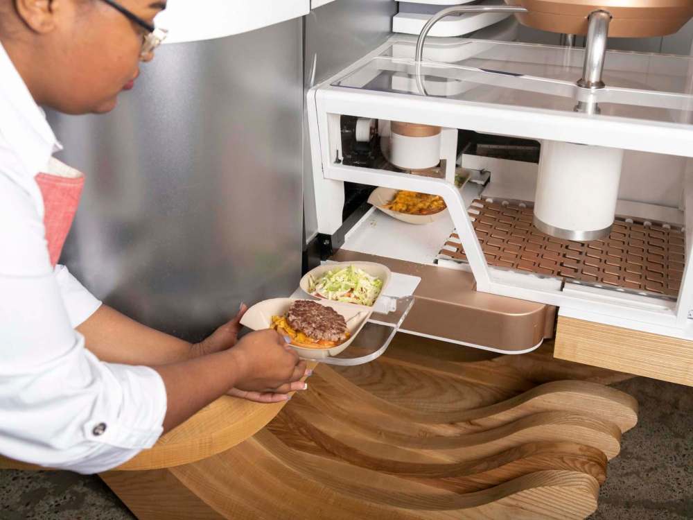 An employee moves an almost completed burger from the machine at the Creator storefront in San Francisco, California, U.S., on Monday, June 18, 2018. On June 27, the world's first robot-crafted burger will roll off a conveyor belt in San Francisco and into the hands of the public. The product, from Bay Area-based Creator, a culinary robotics company, is assembled and cooked in a machine that contains 20 computers, 350 sensors, and 50 actuator mechanisms. Photographer: Cayce Clifford/Bloomberg