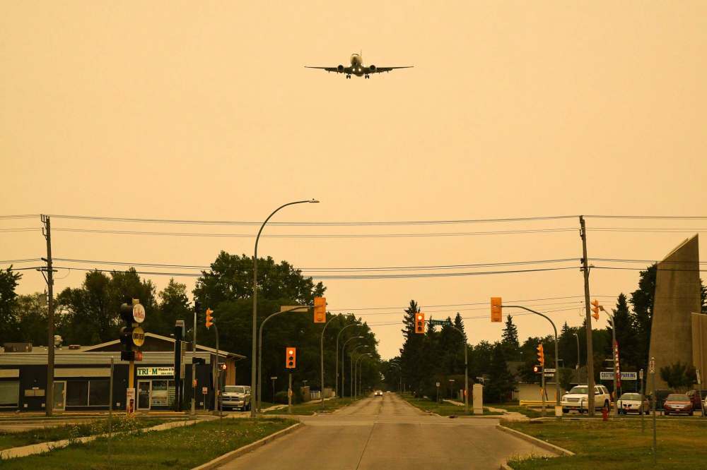 A plane comes in to land through the smoky orange sky over Ness Avenue. (Mike Sudoma / Winnipeg Free Press)