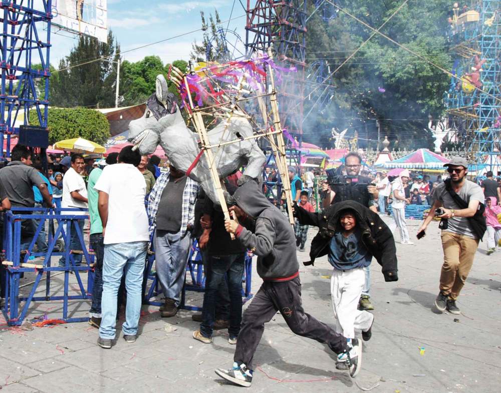 Cameras follow kids as they carry a papier-mâché donkey through the fairgrounds where the Castles of Fire are being assembled. (Oscilloscope)