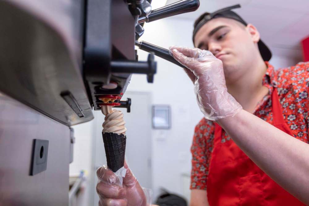 Assistant store manager Alex Berens serves up an orange Creamsicle-flavoured soft serve on top of a black charcoal cone at Teeyah’s Candy, Soda and Ice Cream. (Sasha Sefter / Winnipeg Free Press)