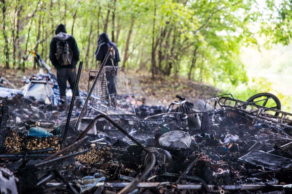 Residents of a homeless encampment under the Osborne Street Bridge look through rubble following a fire Wednesday morning. (Mikaela MacKenzie / Winnipeg Free Press)