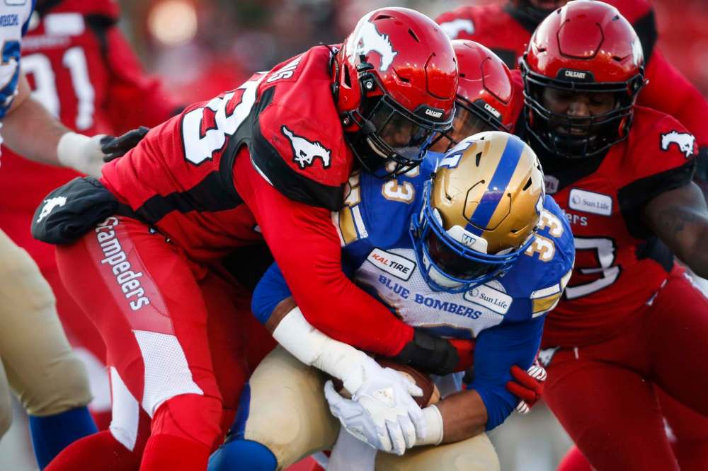 JEFF MCINTOSH / THE CANADIAN PRESS
Winnipeg Blue Bombers' Andrew Harris, centre, is tackled by Calgary Stampeders' Wynton McManis.