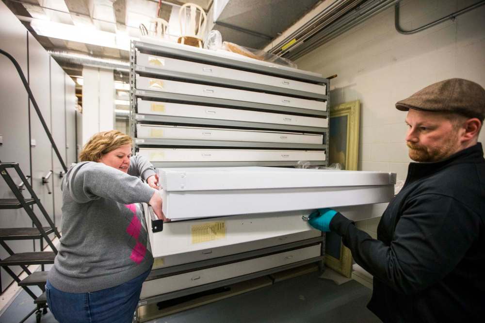 Cindy Colford, manager of collections and conservation at the Manitoba Museum, and Loren Rudisuela, conservation technician, put a Dakota Plains coat into a storage drawer. (Mikaela MacKenzie / Winnipeg Free Press)