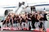 Members of the United States women's soccer team, winners of a fourth Women's World Cup, pose with the trophy by their plane after arriving at Newark Liberty International Airport, Monday, July 8, 2019, in Newark, N.J. Julie Ertz holds the trophy, Megan Rapinoe, front right, gestures, and Alex Morgan, back left, also gestures. (AP Photo/Kathy Willens)