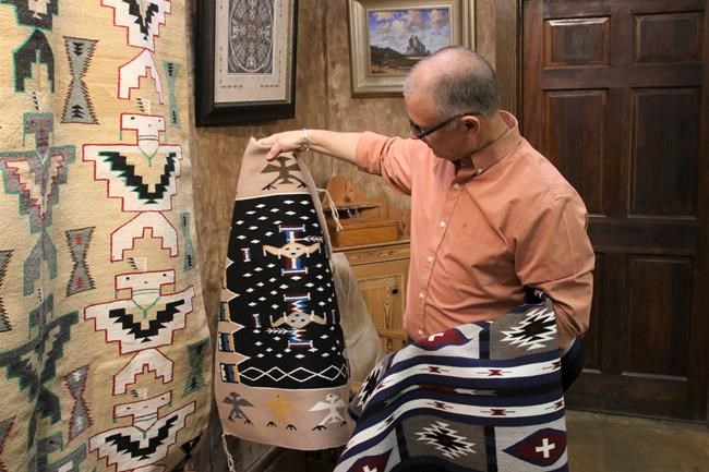 In this May 17, 2019 photo, Shiprock Trading Post owner Kent Morrow looks over rugs at his Farmington, N.M., business that operates under a model much different than the way trading posts traditionally have been run. The trading posts, once a staple in the Four Corners region that connected Navajo weavers and artists to buyers, are facing challenges to their survival. (Mike Easterling/The Daily Times via AP)