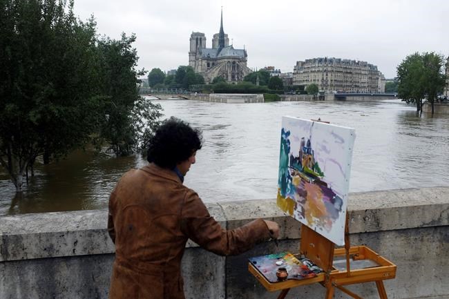 FILE - In this Friday, June 3, 2016 file photo, a man paints the Notre Dame cathedral surrounded by the flooding Seine river in Paris, France. The Gothic structure, which sustained a devastating fire Monday, April 15, 2019, has inspired writers, painters and filmmakers for hundreds of years. (AP Photo/Jerome Delay)
