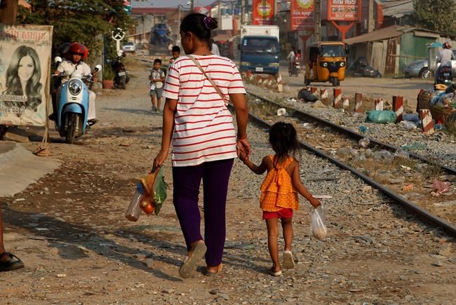 FILE - In this Jan. 29, 2019, file photo a garment worker walks with her child from the factory after her shift in Phnom Penh, Cambodia. In a report Tuesday, Oct. 8, the World Bank warns that trade conflicts between major countries, specifically the United States and China, are disrupting supply chains and causing manufacturers to delay investment decisions to avoid getting caught in a trade-war crossfire. (AP Photo/Heng Sinith, File)