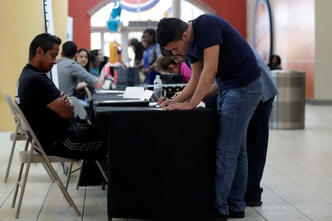 FILE - In this Oct. 1, 2019, file photo Billy Ramos, right, fills out a job application with Adidas during a job fair at Dolphin Mall in Miami. On Friday, Nov. 1, the U.S. government issues the October jobs report. (AP Photo/Lynne Sladky)