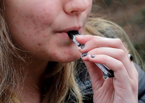 FILE - In this April 11, 2018, file photo, a high school student uses a vaping device near a school campus in Cambridge, Mass. U.S. health regulators are moving ahead with a plan to keep e-cigarettes out of the hands of teenagers by restricting sales of most flavored products in convenience stores and online. (AP Photo/Steven Senne, File)