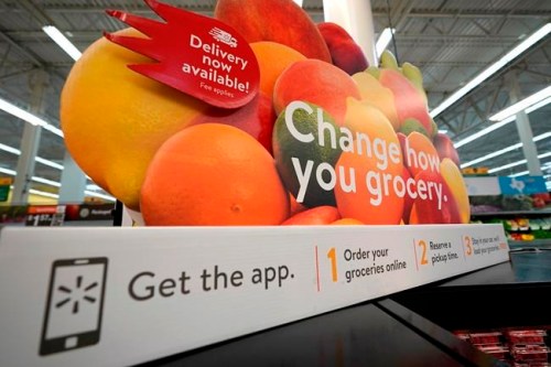 FILE- In this Nov. 9, 2018, file photo a sign promotes online and home delivery of groceries at a Walmart Supercenter in Houston. Retailers are taking back some control of the store experience with smart phone app features that let customers do things like scan and pay and download digital maps. (AP Photo/David J. Phillip, File)