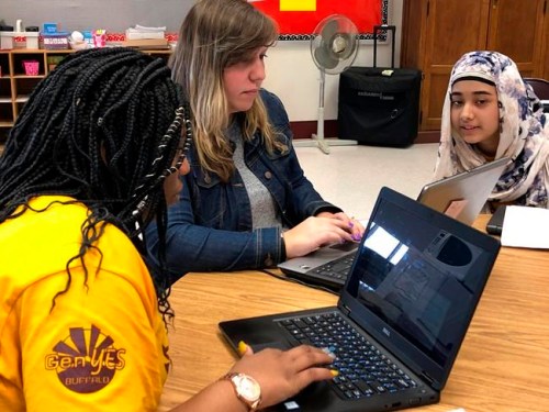 In this April 16, 2019, photo, eighth grade student technicians Mirakle Singleton, left, and Naureen Unaysa, right, instruct teacher Kaila Burgio in the use of a computer program at Buffalo Public School No. 37, in Buffalo, N.Y. The district and others around the country are training students to help with software and hardware issues that arise as teachers and students do more of their daily schoolwork on school-issued laptops and iPads. (AP Photo/Carolyn Thompson)