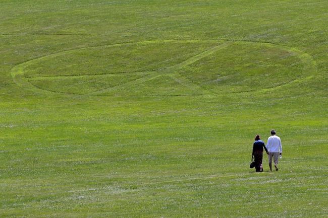 Carol Laura, left, and George Acquaire walk barefoot to a peace sign mowed in the grass at the site of the 1969 Woodstock Music and Arts Fair, Wednesday, July 24, 2019 in Bethel, N.Y. Woodstock will be celebrated on its 50th anniversary, but it won't be your hippie uncle's trample-the-fences concert. While plans for a big Woodstock 50 festival collapsed after a run of calamities, the bucolic upstate New York site of the 1969 show is hosting a long weekend of events featuring separate shows by festival veterans like Carlos Santana and John Fogerty. (AP Photo/Seth Wenig)
