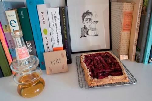 In this May 17, 2019 photo, a rhubarb tart is displayed with a caricature of Jonah Reider and his cookbooks in his New York apartment. In the competitive food world, Reider is a millennial whose cooking is opening doors to adventures far beyond food. (AP Photo/Mary Altaffer)