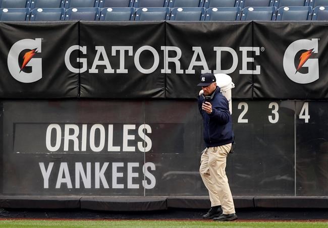 A worker snaps a cell phone photo of the tarp-covered field at Yankee Stadium as he carries a bucket back past the outfield scoreboard after a baseball game between the New York Yankees and the Baltimore Orioles was postponed due to inclement weather, Tuesday, May 14, 2019, in New York. It was the second consecutive day a game between the two teams was postponed. Monday's game was postponed due to unplayable field conditions, specifically a rain-soaked field. (AP Photo/Kathy Willens)