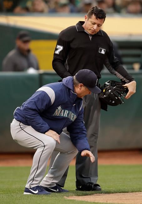 Seattle Mariners manager Scott Servais, left, squats at home plate as he speaks with umpire Carlos Torres in the fourth inning of a baseball game against the Oakland Athletics, Saturday, June 15, 2019, in Oakland, Calif. Servais was ejected from the game by Torres. (AP Photo/Ben Margot)
